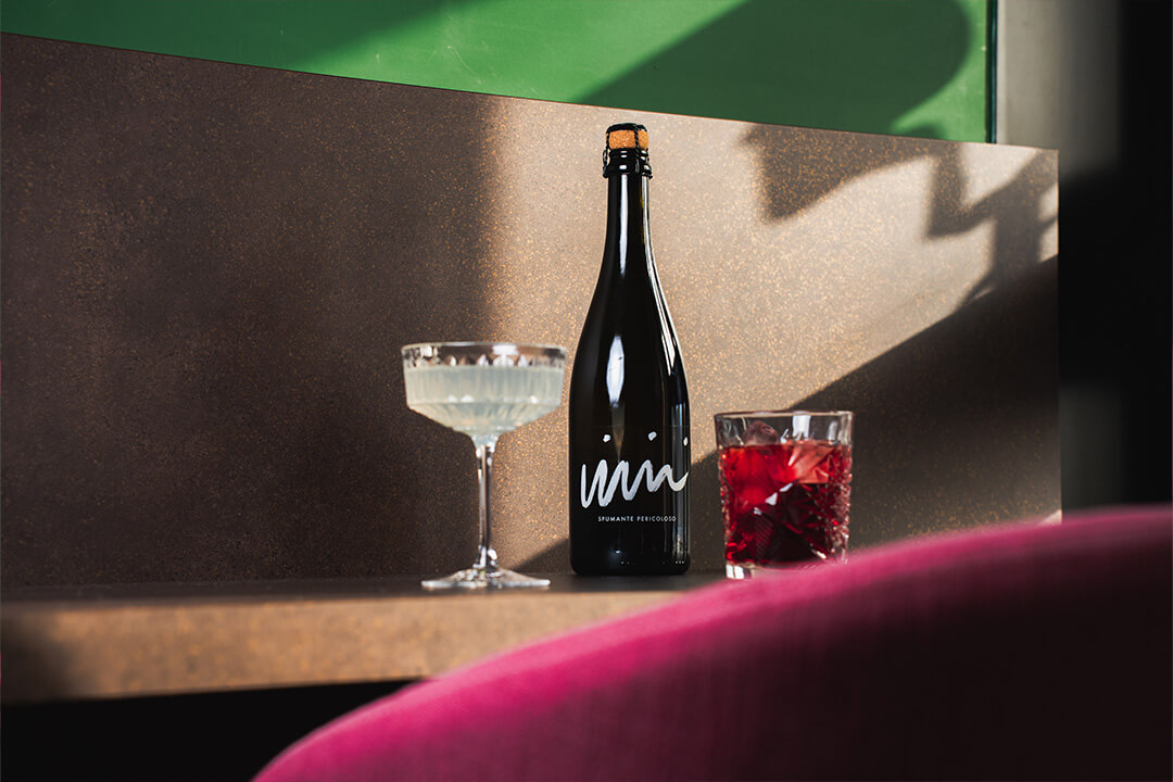 Eine schwarze Flasche mit zwei Gläsern, ein Champagnerglas und ein Stielglas mit rotem Getränk.