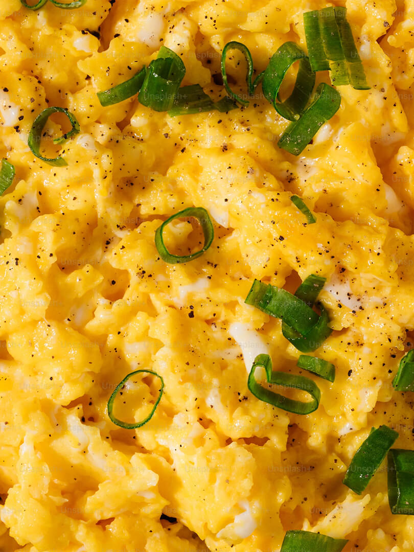 Nahaufnahme von Rührei mit frisch geschnittenen Frühlingszwiebeln und gemahlenem schwarzem Pfeffer.