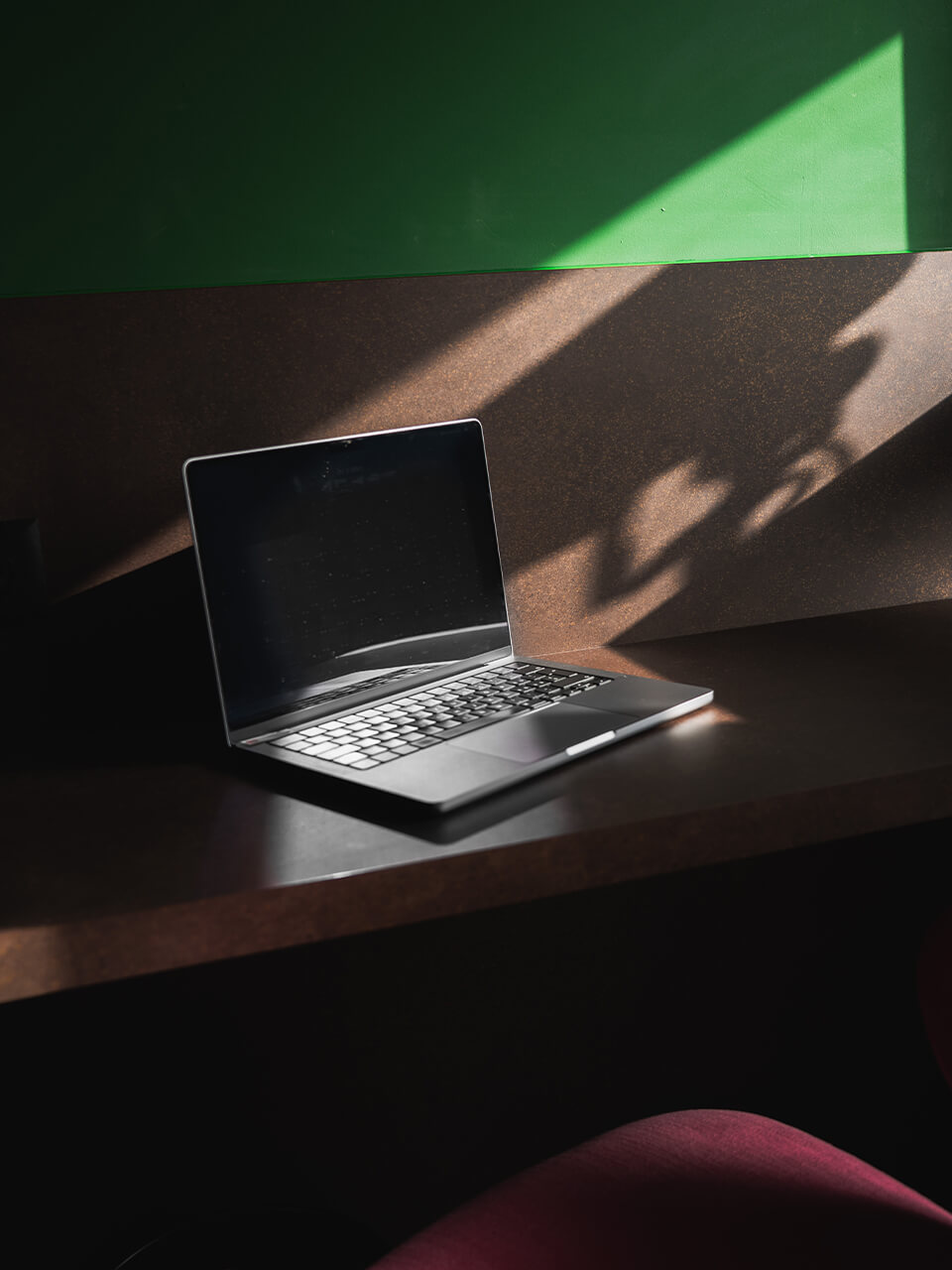 Ein Laptop steht auf einem Tisch mit Sonnenlicht und Schatten an einer grünen Wand.