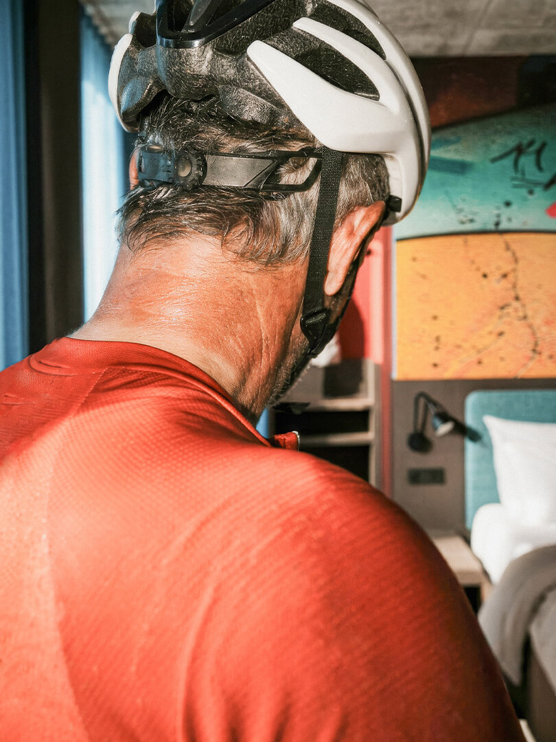 Mann mit hellem Radhelm und rotem Hemd schaut in ein Zimmer mit Bett und Wandbild.