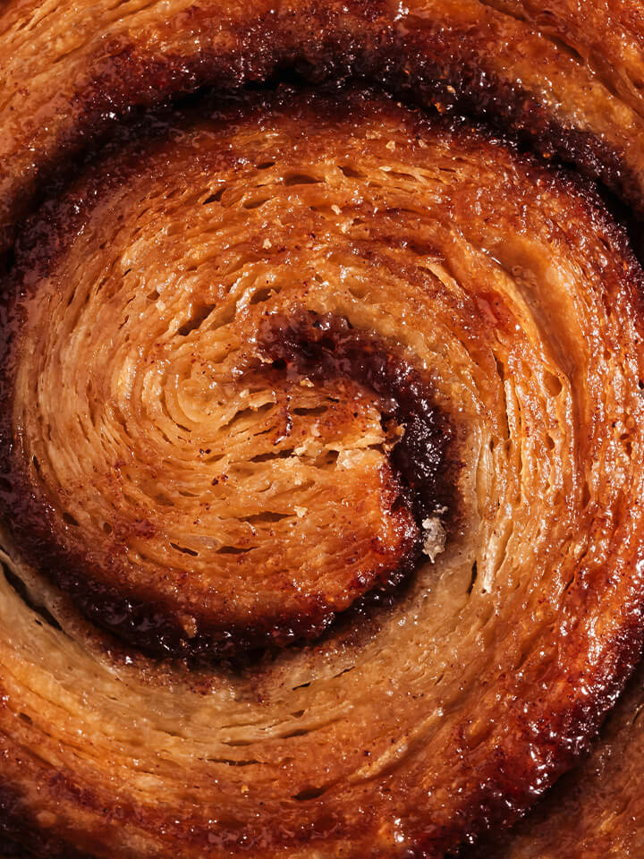 Nahaufnahme eines goldbraunen, knusprigen Zimtschnecken-Gebäcks mit Zimtfüllung.
