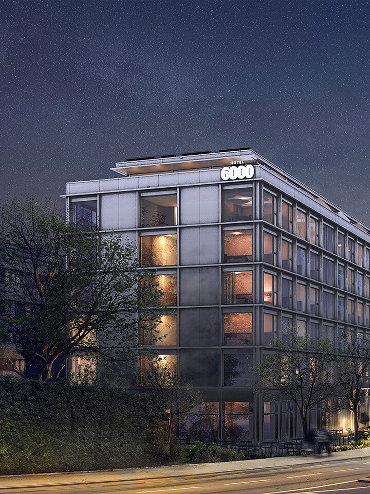 Das Hotel 6000-Gebäude bei Nacht mit beleuchteten Fenstern; auf der Strasse gehen mehrere Personen.