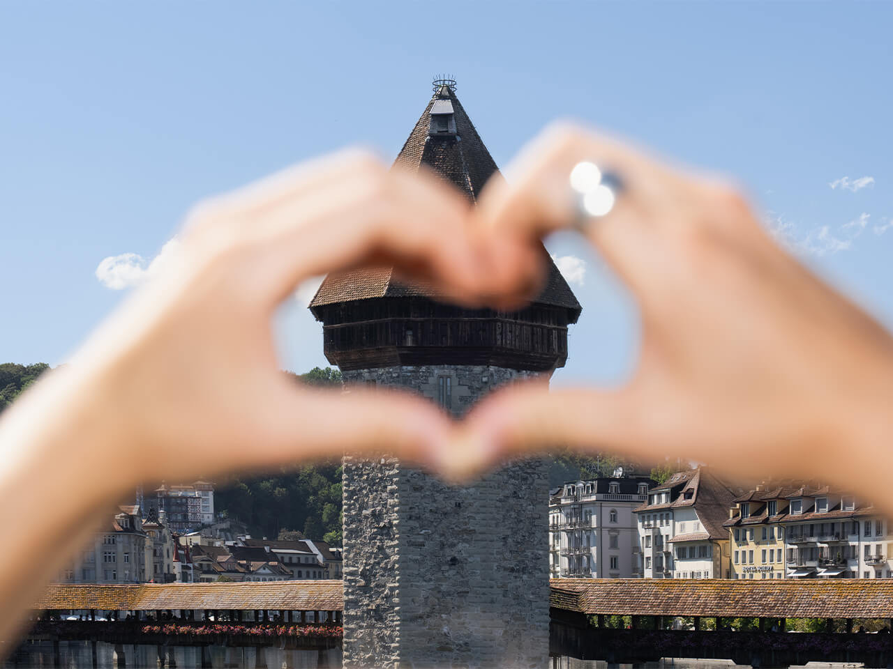 Hände formen ein Herz vor dem steinernen Wasserturm und der Kapellbrücke in Luzern.