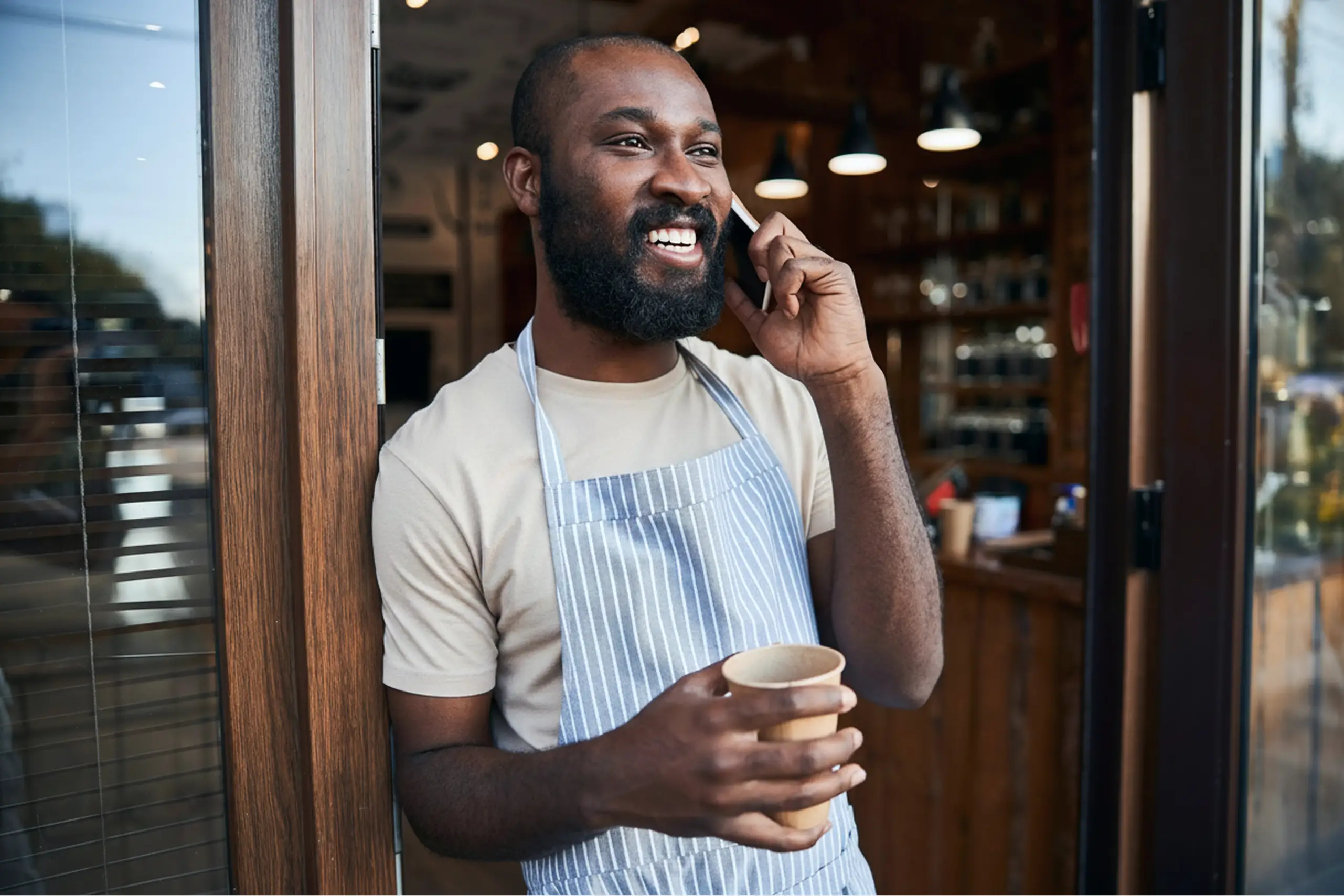 A man standing talking on a cellphone and holding a paper cup.