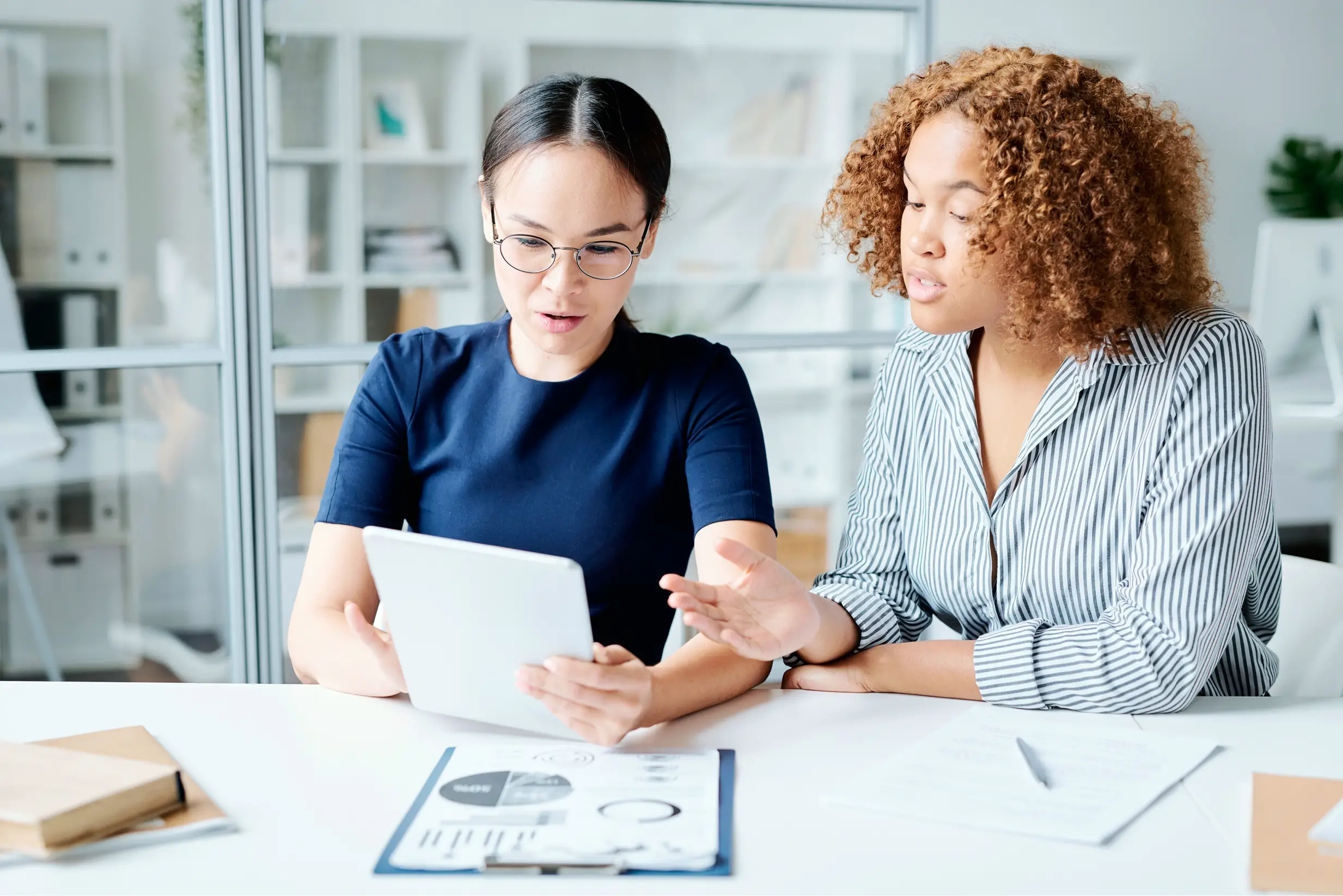 Two women talking while looking at a tablet.