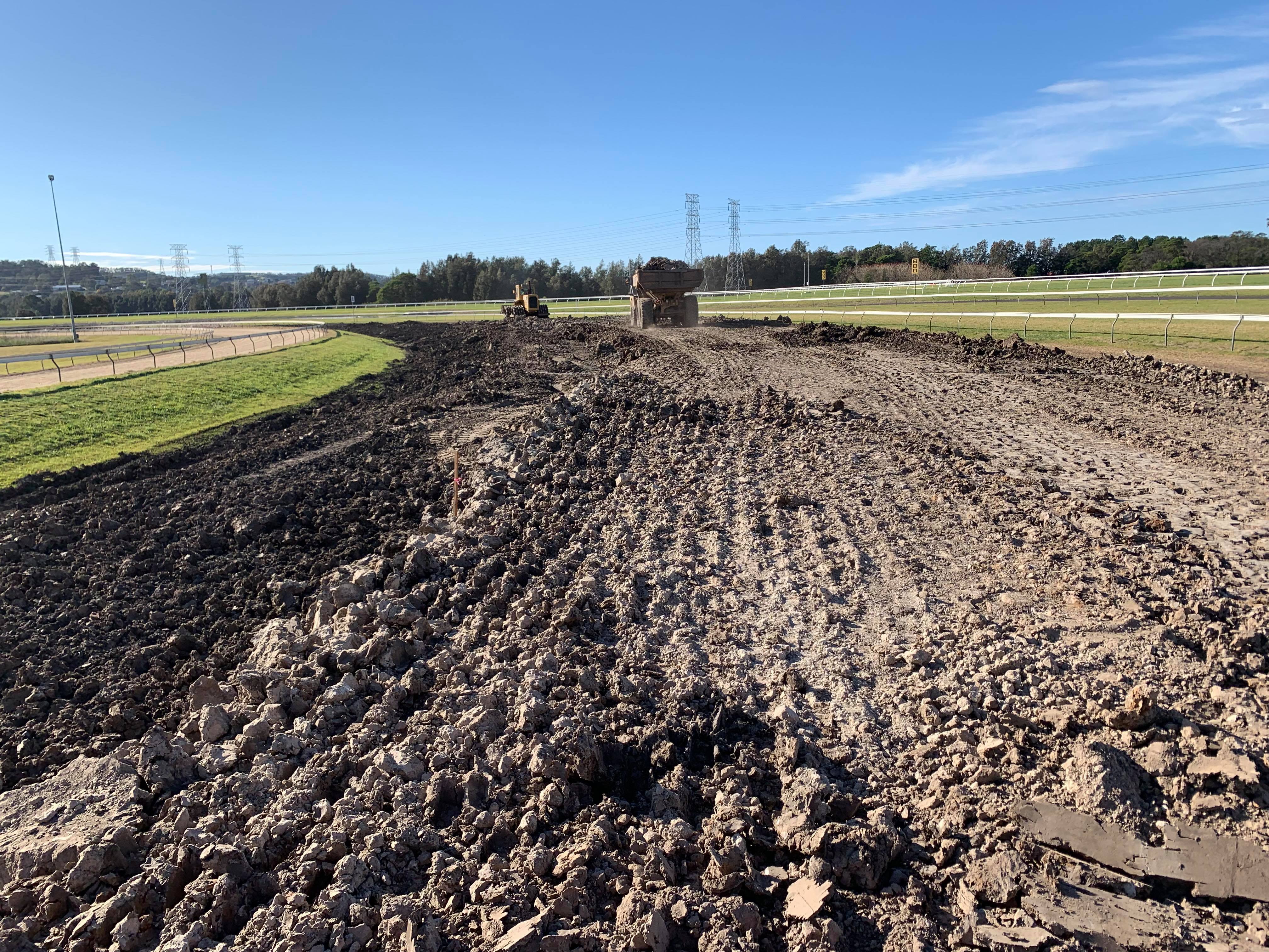 Construction vehicles leveling and working on a large dirt track under a clear blue sky.