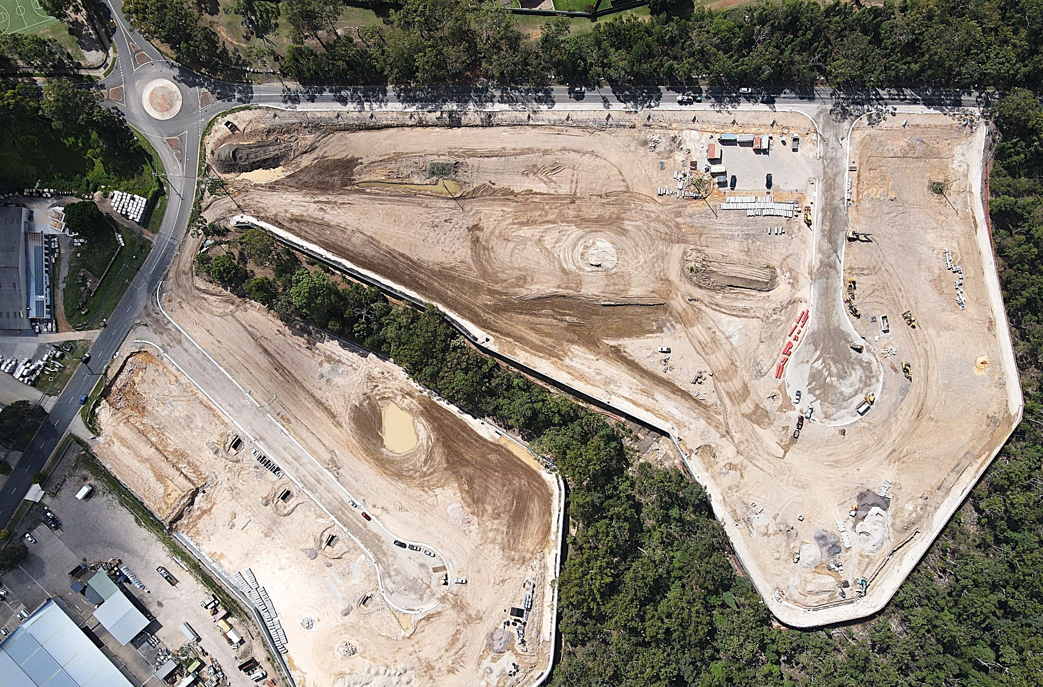Aerial view of a large construction site surrounded by trees with cleared land, dirt roads, and construction vehicles.