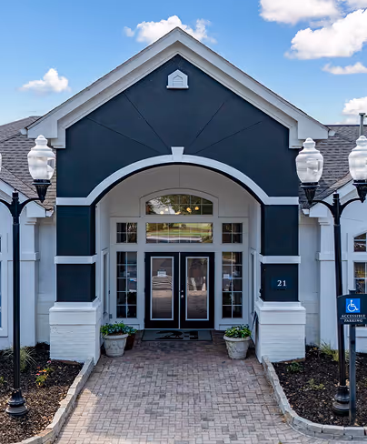 Entrance of a building with double glass doors, black and white archway, potted plants, and accessible parking sign.