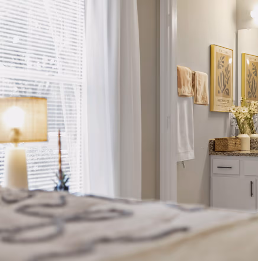 Bright bathroom with beige walls, granite countertop with floral decor, and two framed botanical prints above a white cabinet.