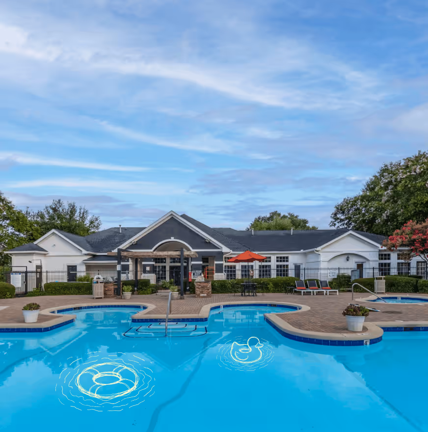 Outdoor swimming pool with seating area and residential buildings under a blue sky.