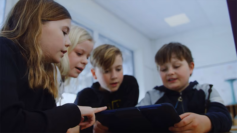 Fire barn ser på og bruker et nettbrett sammen i et lyst klasserom.