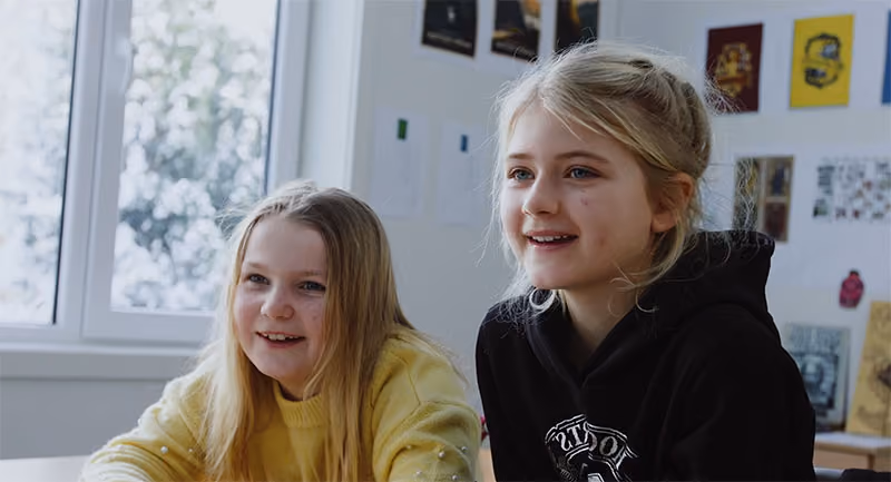 To elever følger med og smiler i klasserommet
