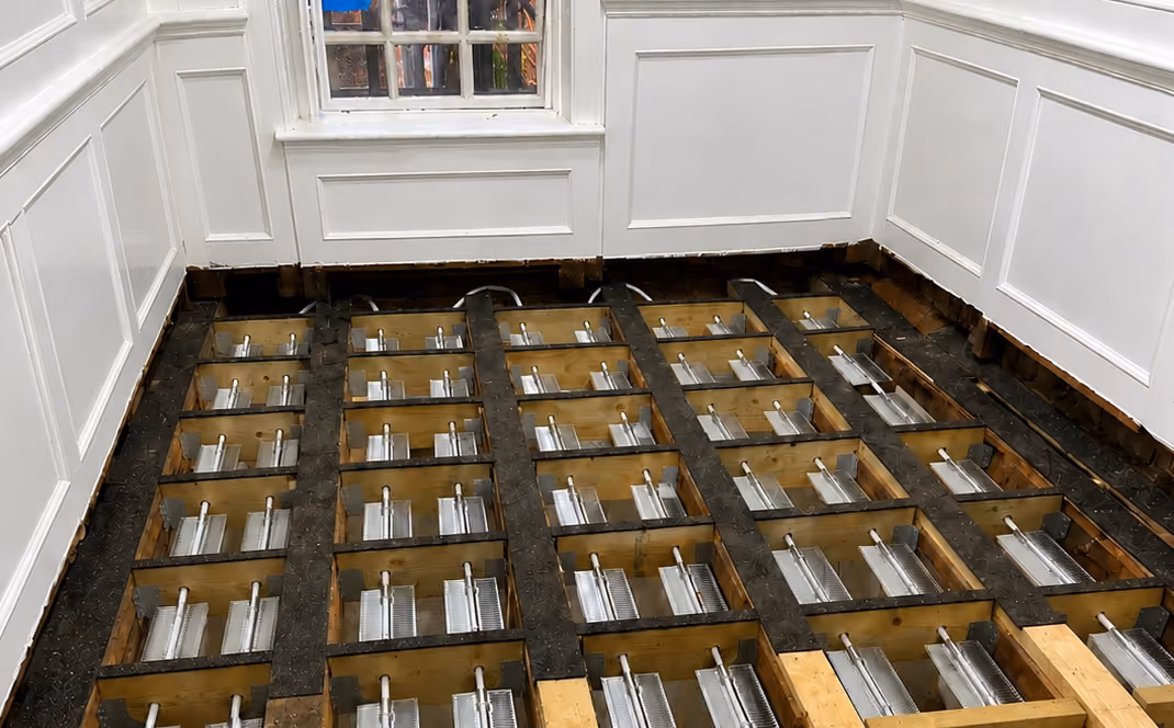 Wooden floor framework with metal fasteners inside an empty room with white paneled walls.