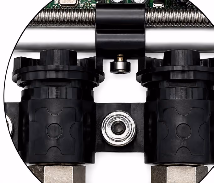 Close-up of two black plastic valves connected by a metal and plastic structure on a white background.