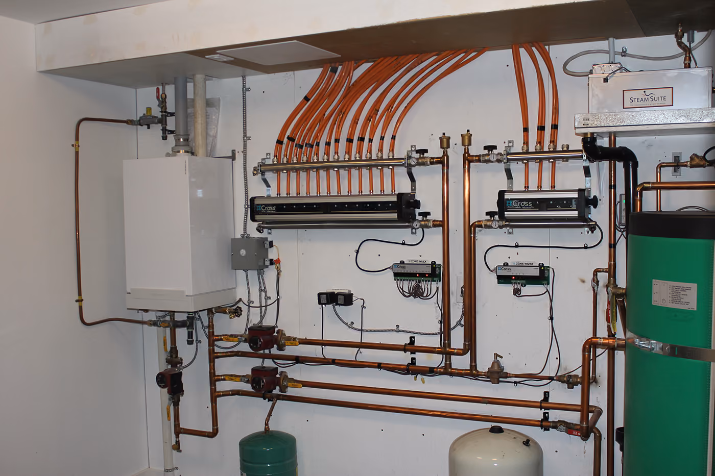 Heating system pipes, pumps, and control units mounted on a wall in a utility room.