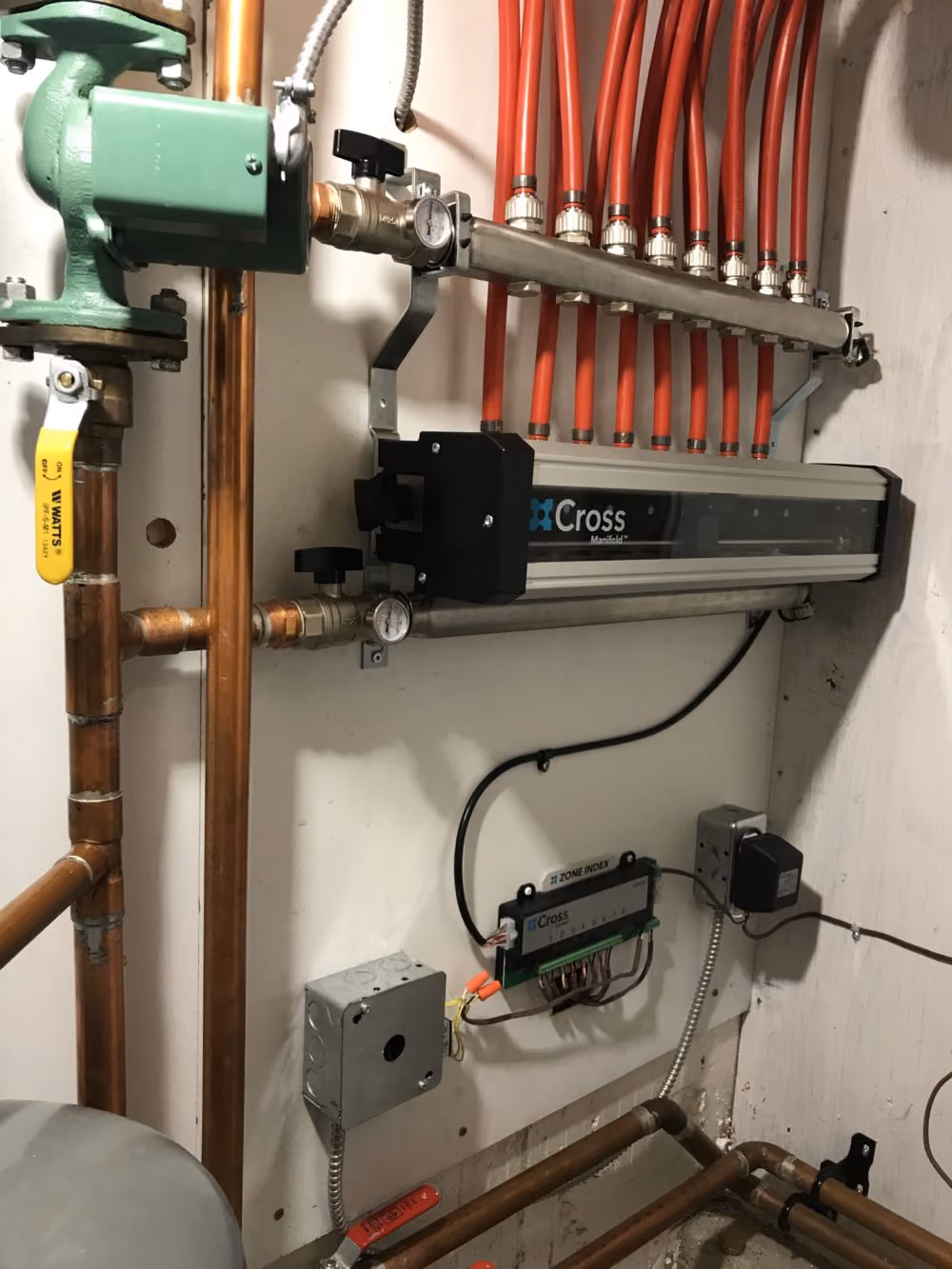 Cross Manifold plumbing setup with red tubes, copper pipes, valves, and electrical control mounted on wall.