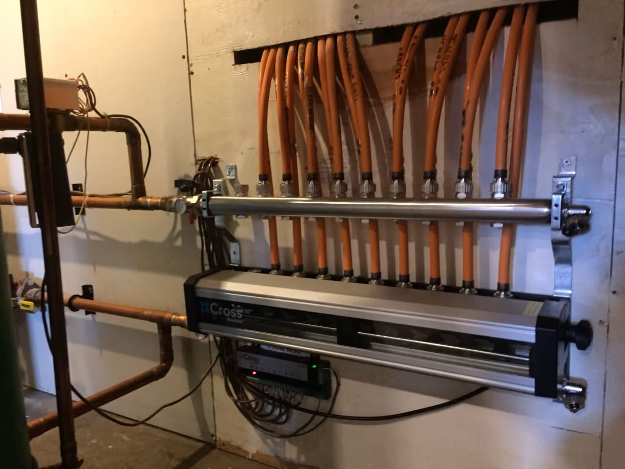 Wall-mounted manifold system with orange tubing and pipes connected for fluid distribution.