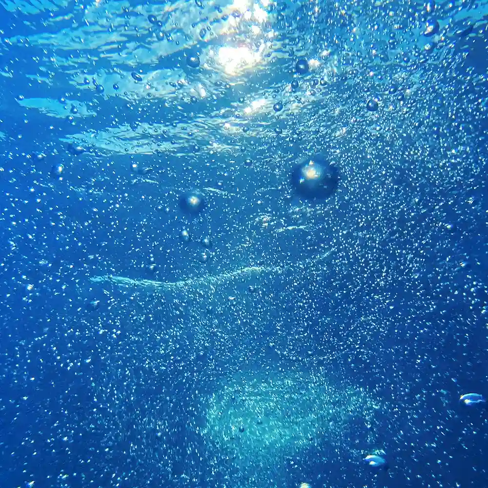 Burbujas ascendiendo bajo el agua iluminada por el sol