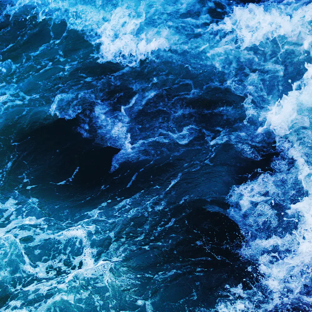 Vista aérea de olas y espuma sobre agua azul intensa