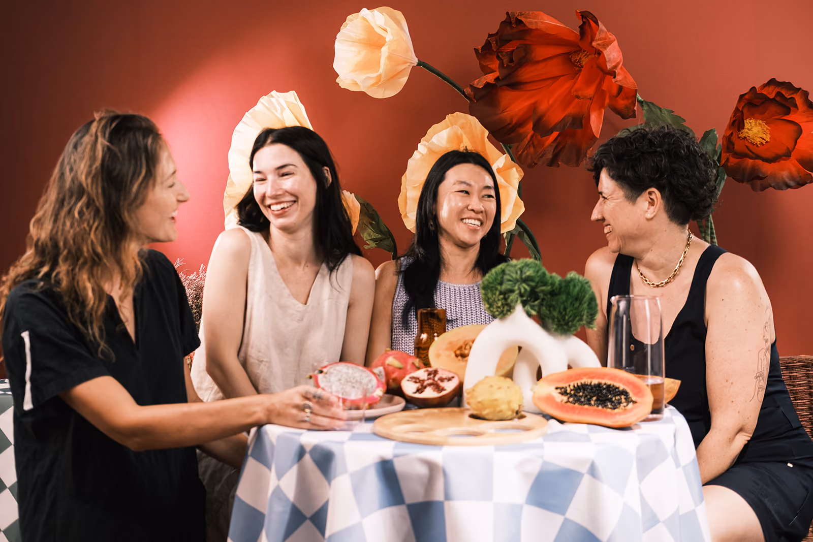 Three women laughing and hugging each other in casual clothing against a light background.