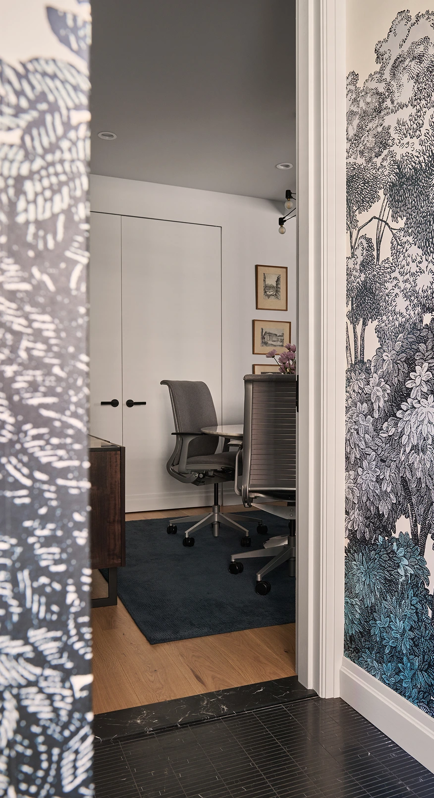 Modern office with two gray swivel chairs, a round table, and detailed black-and-white wallpaper.