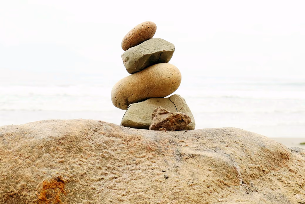 Stack of five balanced stones on a large rock with a blurred ocean background.
