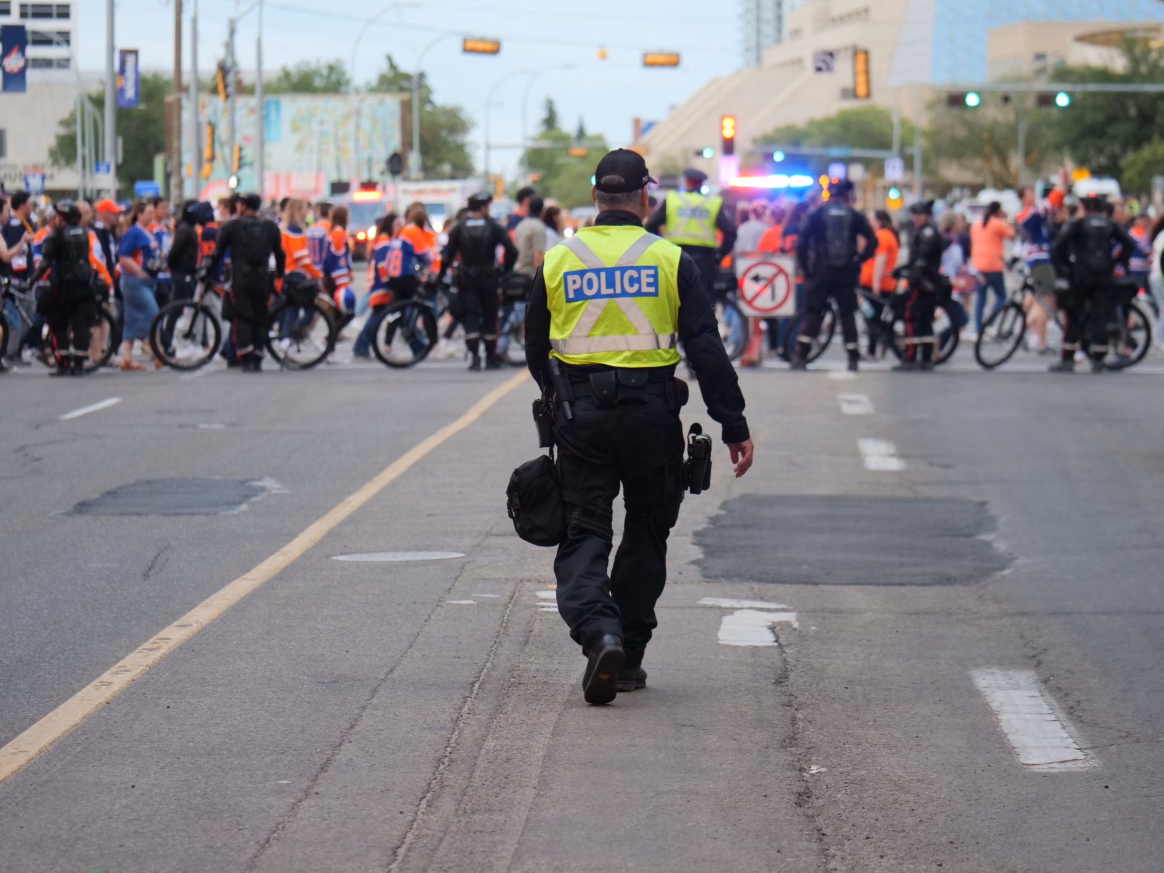 Edmonton Police officer in yellow vest walking toward a crowd and other officers on a Edmonton city street.