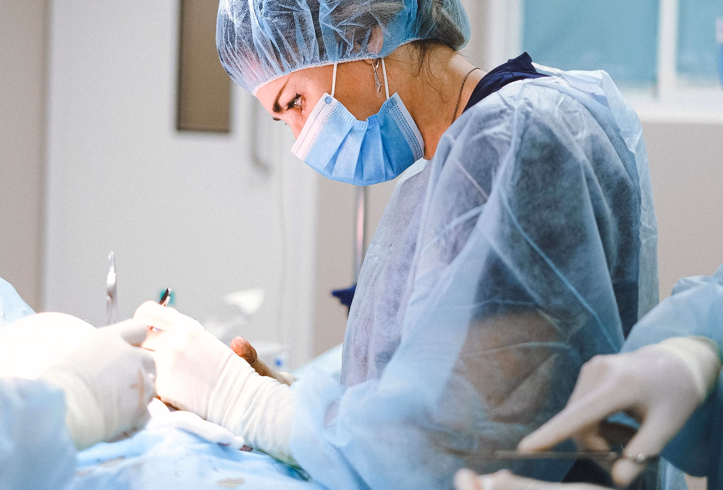 Edmonton Emergency surgeon and nurse wearing surgical mask, cap, and gown performing operation in sterile medical environment.