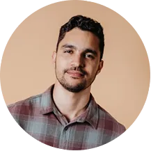 Man with short black hair and beard wearing a plaid shirt against a beige background.
