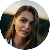 Portrait of a young woman with long brown hair, light makeup, and a gentle smile, outdoors at sunset.