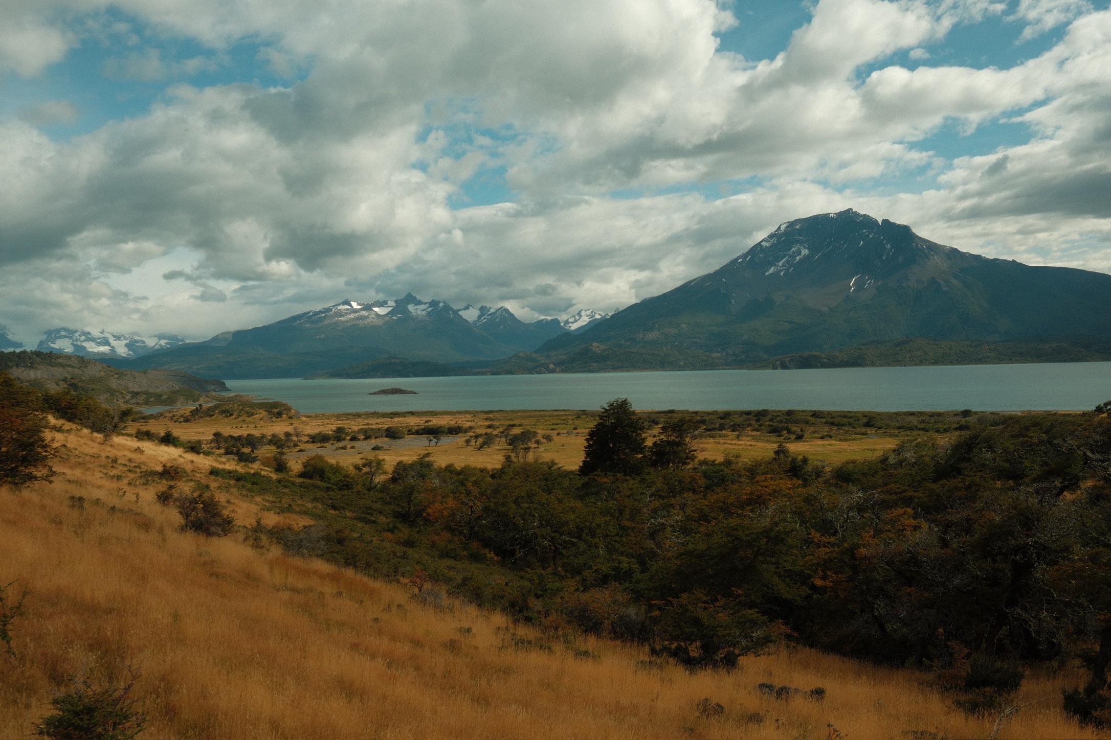 Turquoise Patagonian lake beneath snow-covered peaks and golden grass
