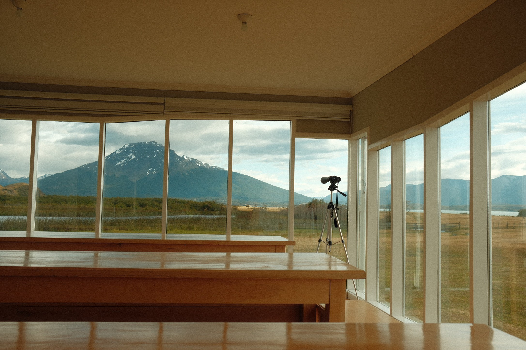 Spotting scope on a tripod aimed at a Patagonian mountain through lodge windows