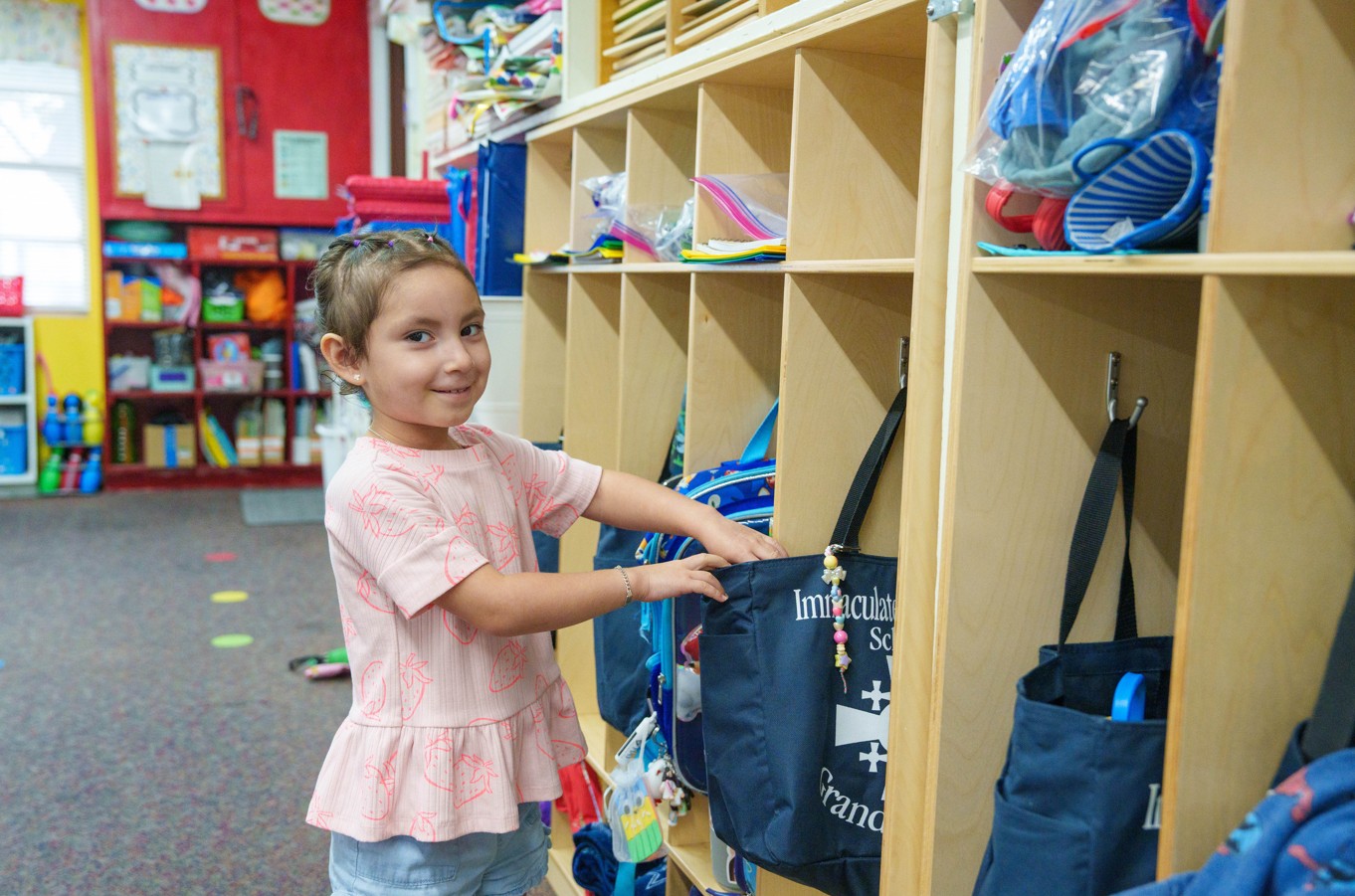Young girl retrieving her bag from classroom cubby hooks
