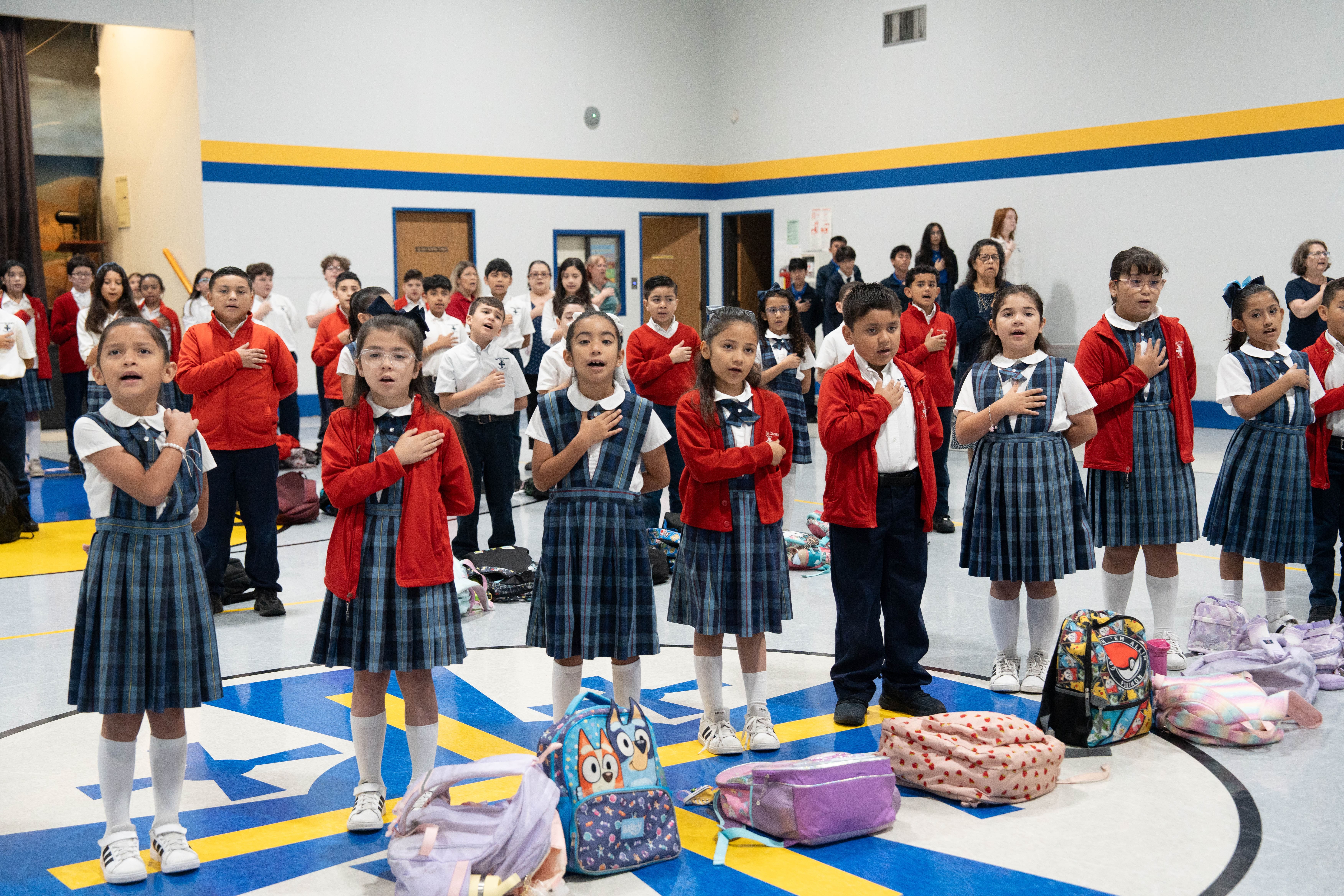 Students in uniform reciting the Pledge of Allegiance in school gymnasium