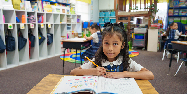 Elementary student in uniform writing in a workbook at her desk