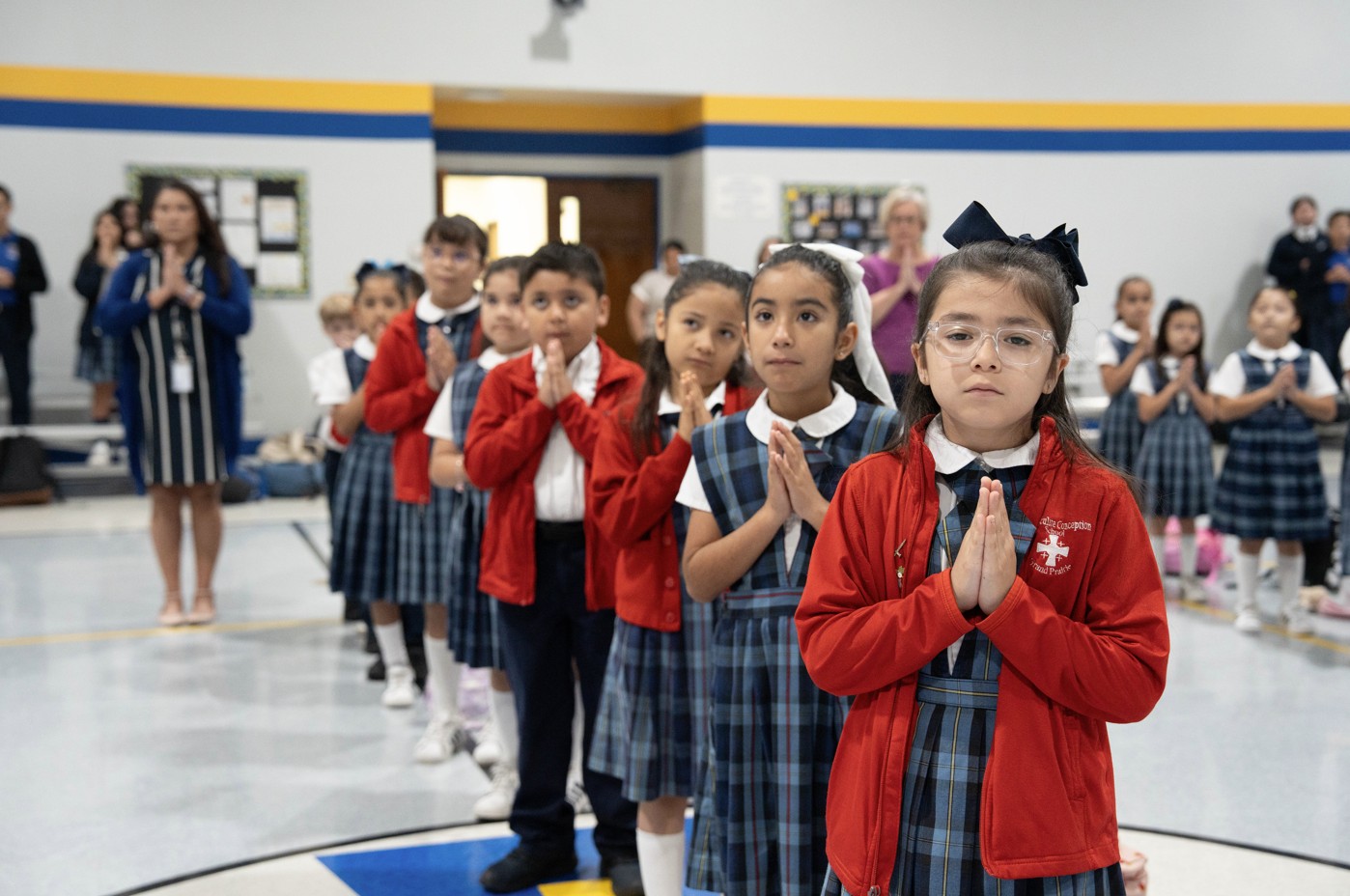 Catholic school students in uniform praying together in gymnasium
