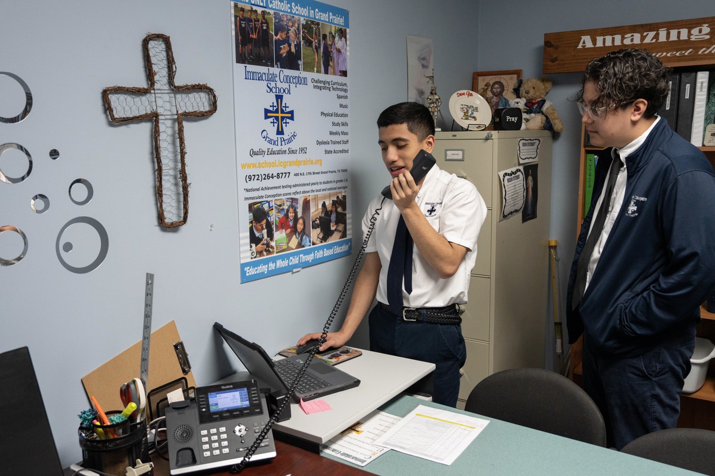 Two uniformed students working at an office desk with phone