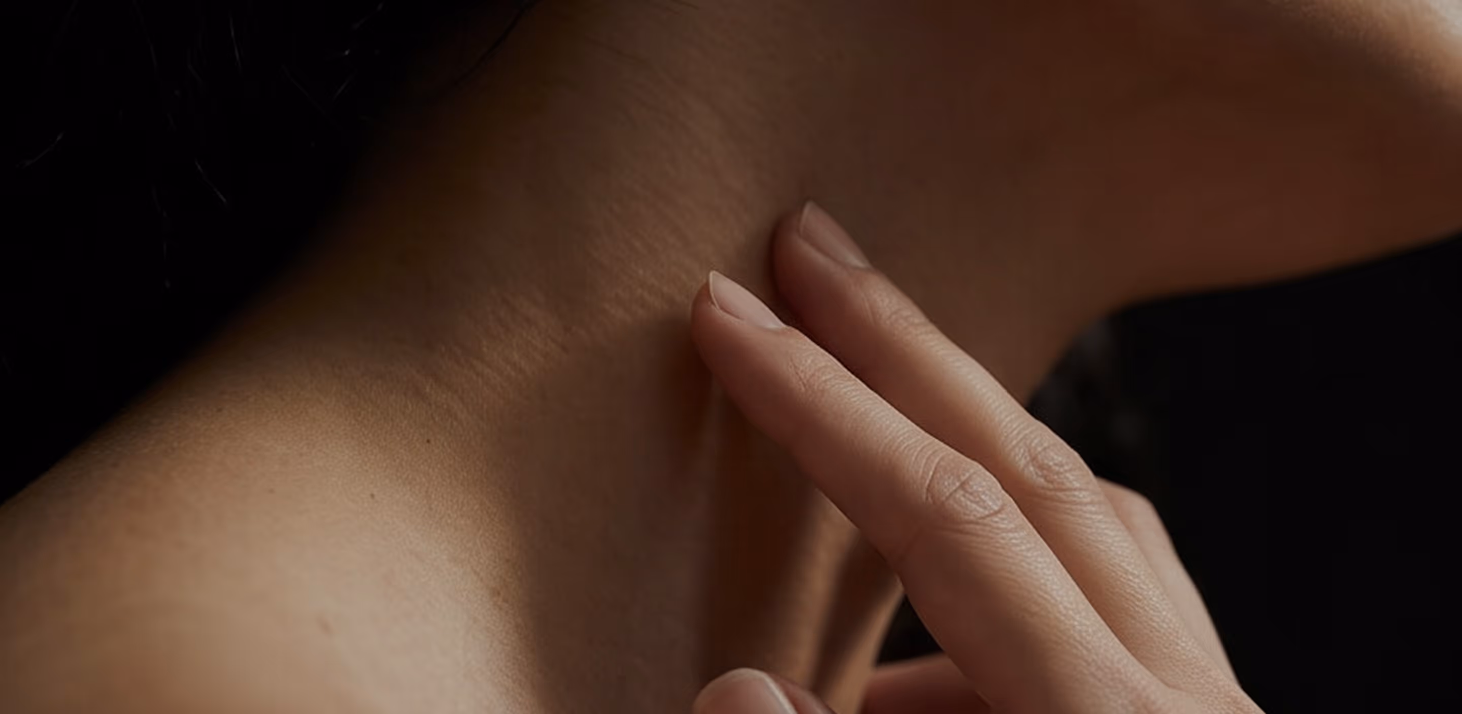 Close-up of a hand gently touching the side of a person's neck against a dark background.