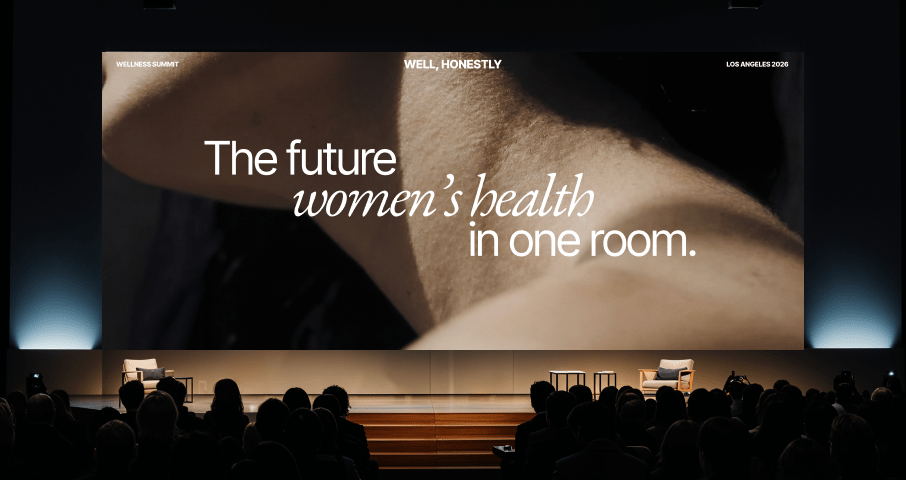 Audience watching a large screen displaying a woman’s neck and shoulder with text about women's health conference.