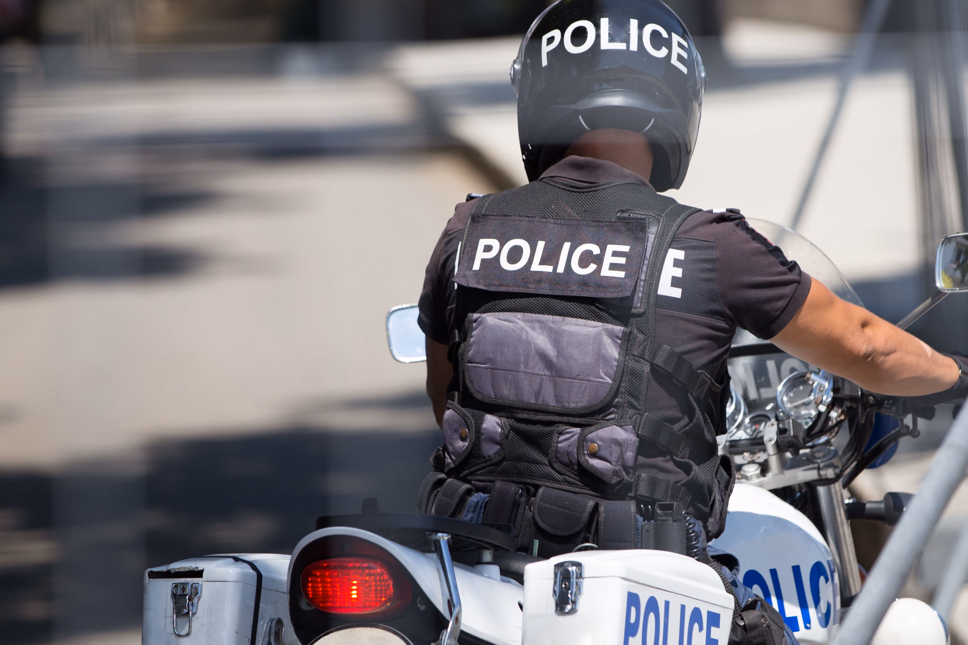 Police officer wearing a helmet and vest riding a white police motorcycle on a street.