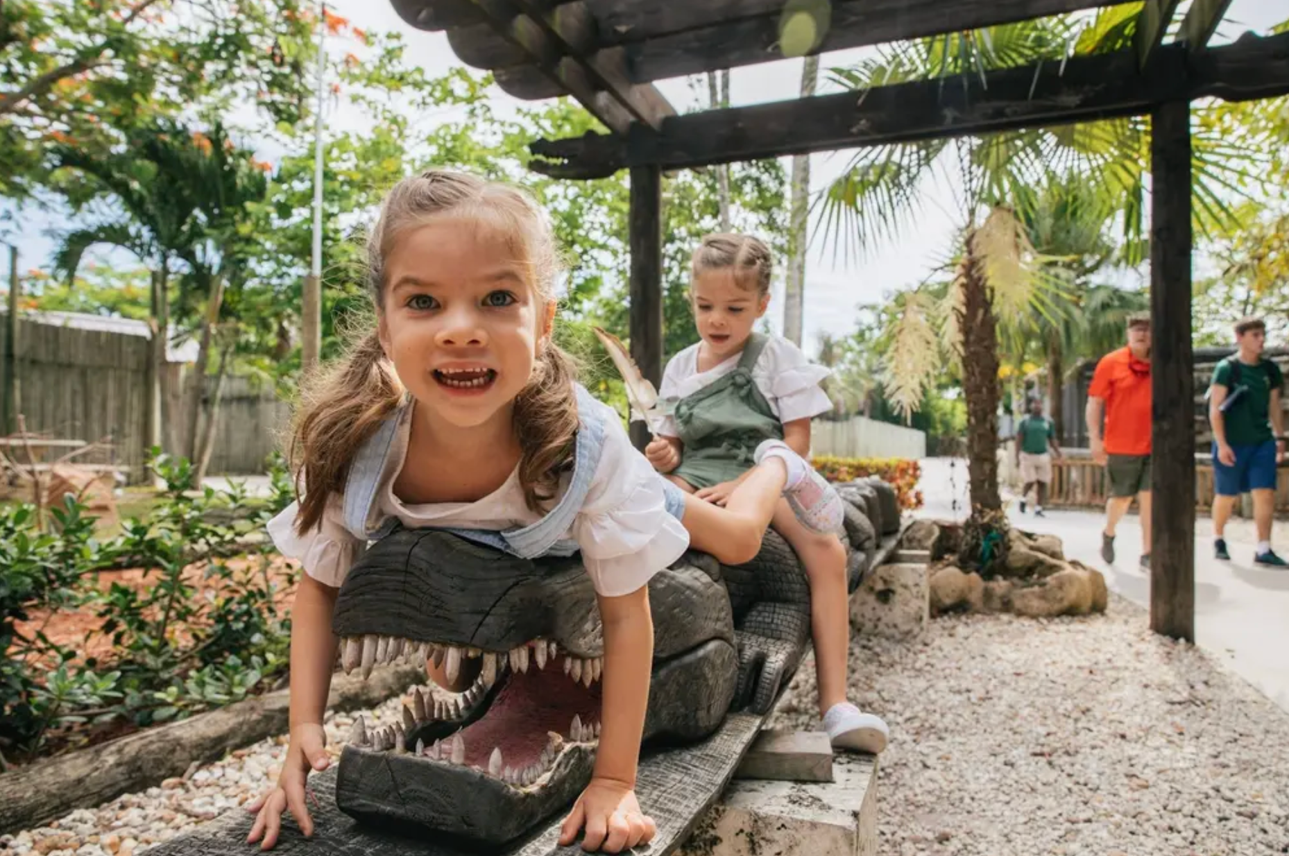 Two young girls climbing on an alligator sculpture while exploring the grounds at Everglades Alligator Farm