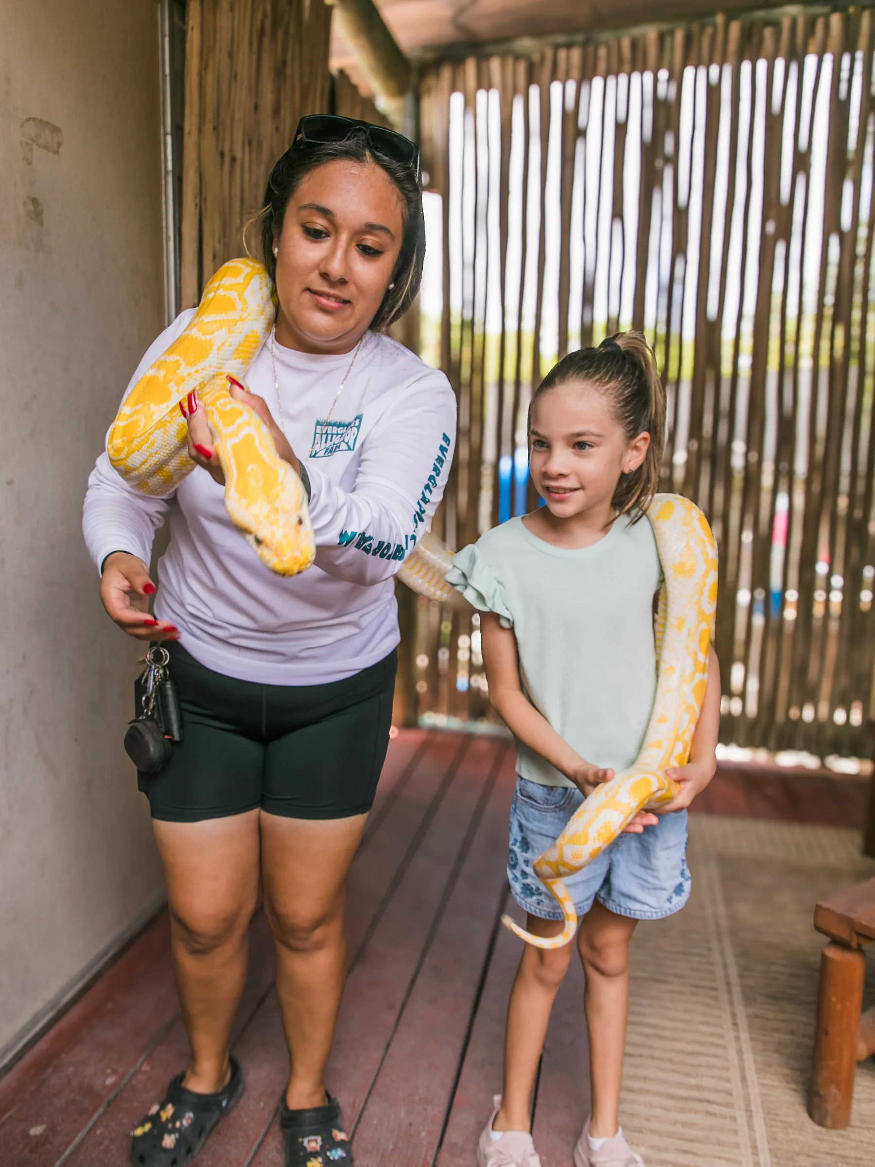 Animal team member wearing an albino python across her shoulders beside a young guest on the reptile deck