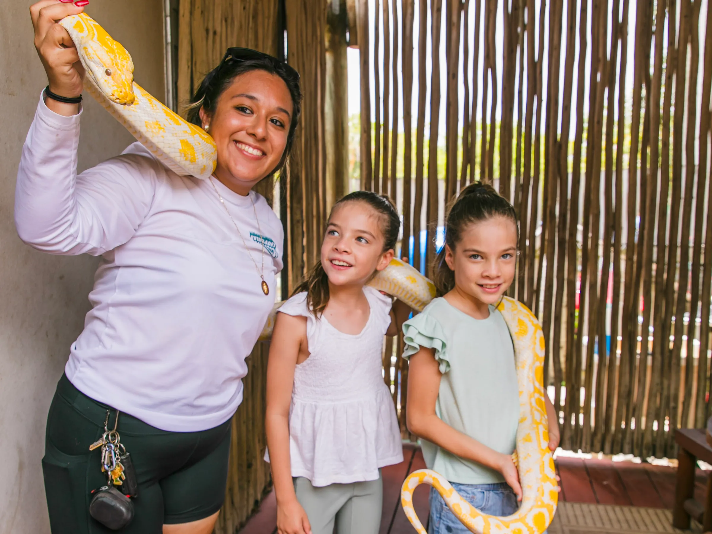 Two girls smiling next to an animal team member holding an albino python at Everglades Alligator Farm