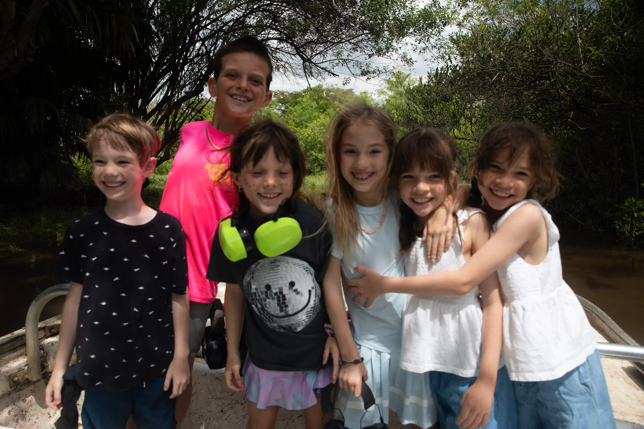 Group of smiling kids on an airboat along a tree lined Everglades waterway
