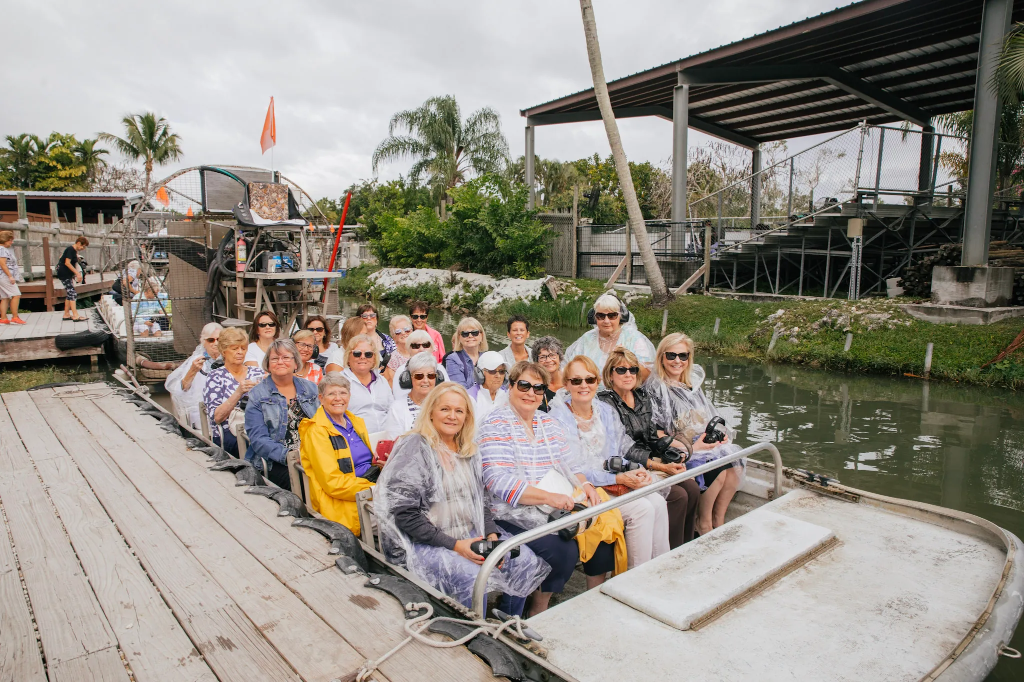 Large group of guests in rain ponchos seated on an airboat at the dock before an Everglades ride