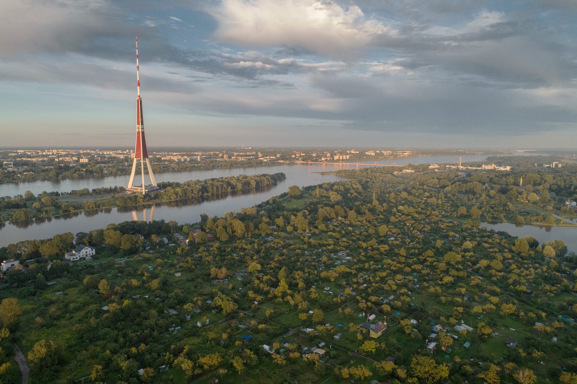 Lucavsala no gaisa: mazdārziņu lauki Daugavas vidū, fonā Rīgas radio un televīzijas tornis un pilsētas panorāma