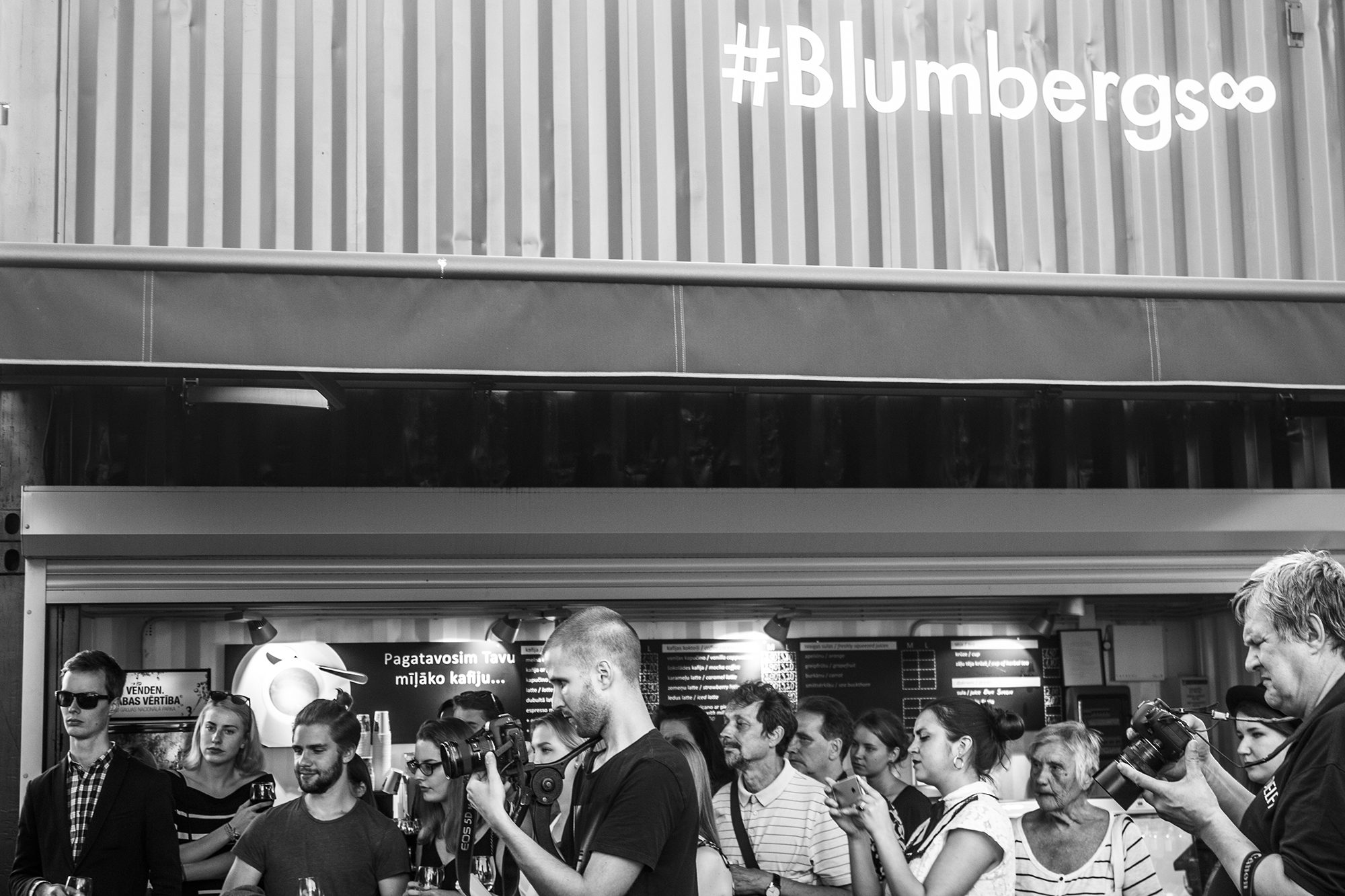 Apmeklētāju pulks zem konteinera ar uzrakstu „#Blumbergs∞“