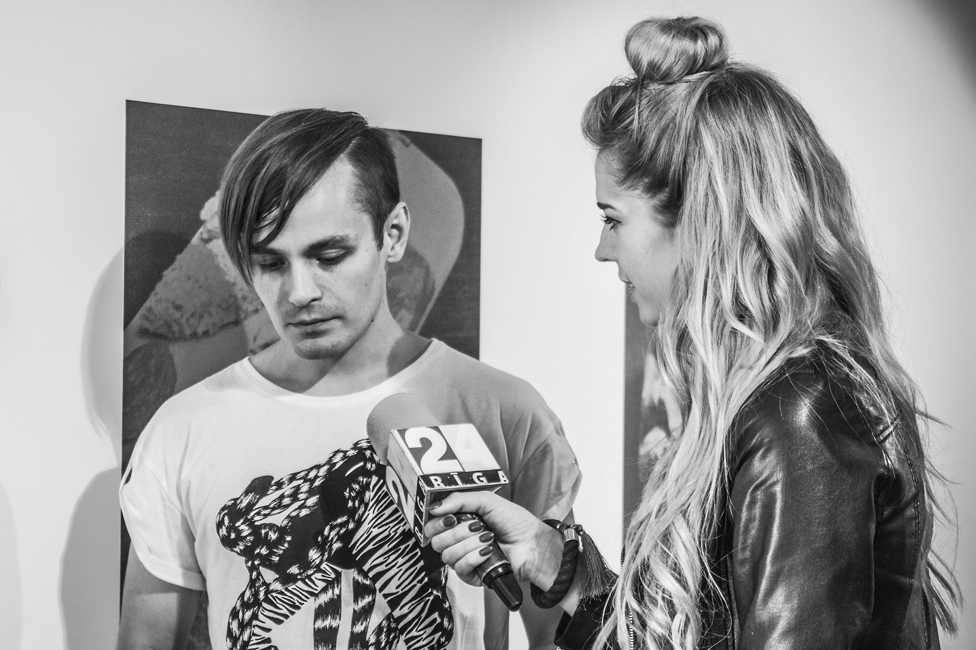 Vīrietis sniedz interviju; sievietei rokā mikrofons ar „Rīga TV24“ logotipu