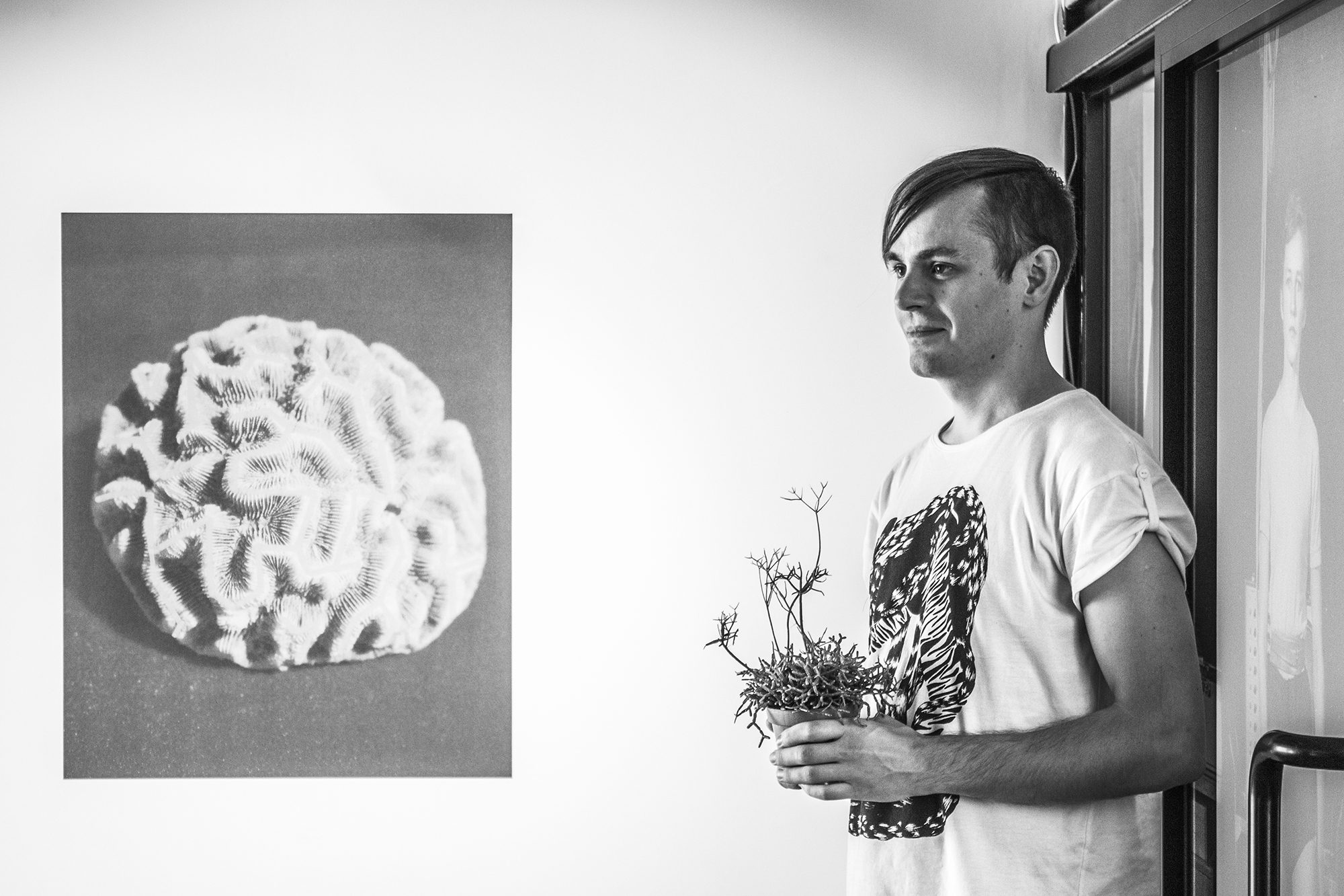 Kolāža ar smadzeņveida formu uz tumša fona; blakus stāv vīrietis ar ziedu pušķi rokās