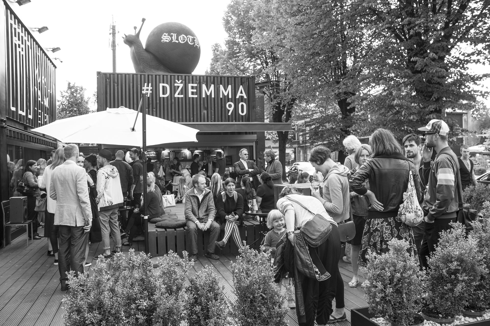 Apmeklētāji pulcējušies uz terases pie konteinera ar uzrakstu „#Džemma 90”